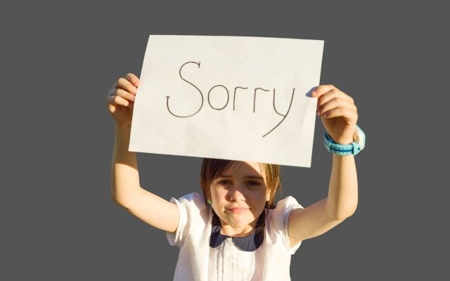 a girl holding an apology board with both of her hands