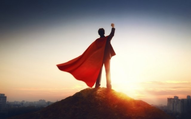 superman standing on top of a hill and raising his right hand making a fist